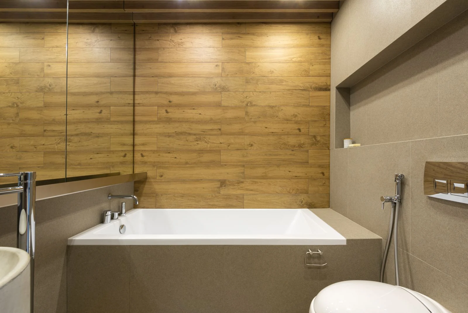 Interior of modern bathroom with mirror hanging above sink and bathtub near toilet and bidet spray