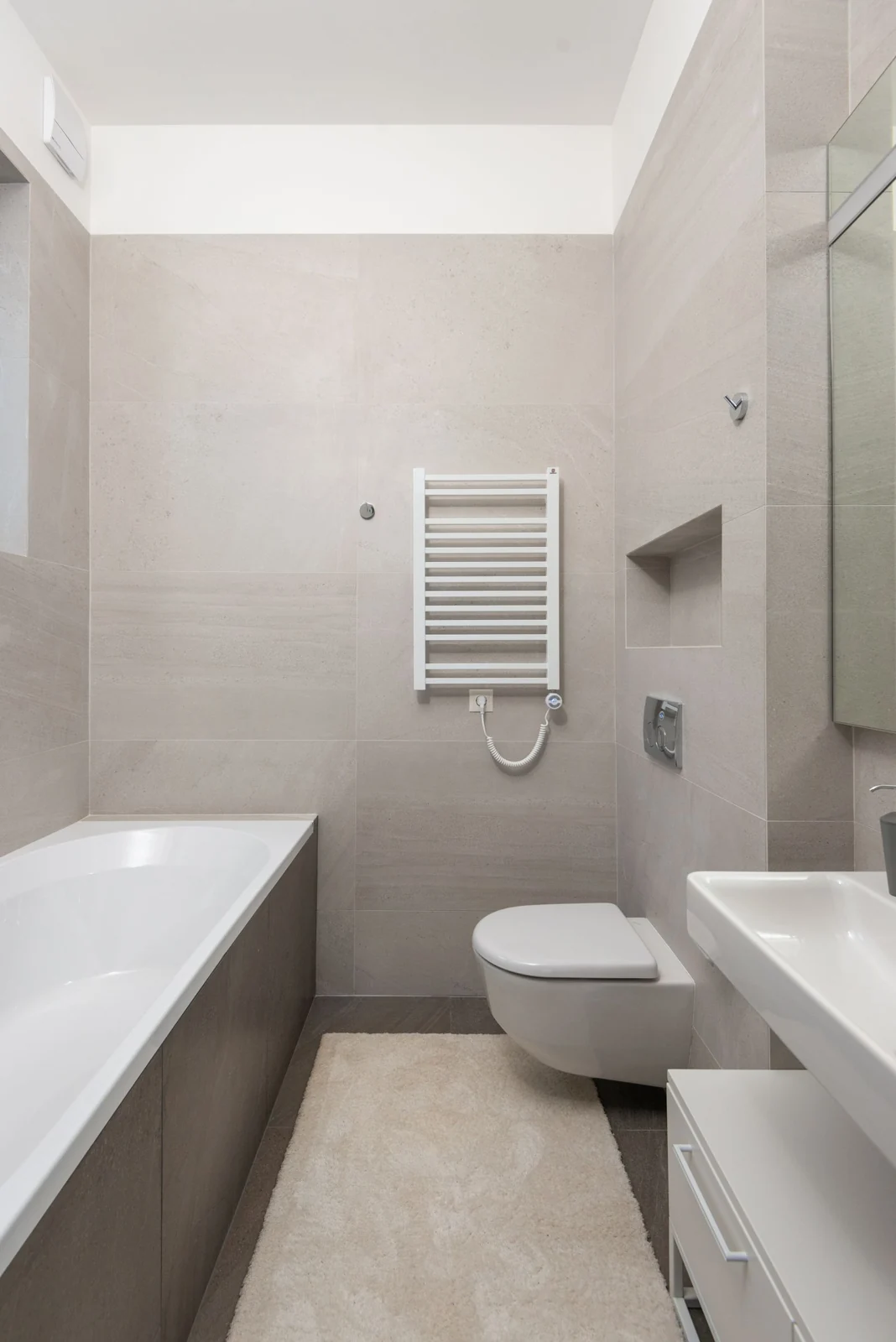 Ceramic bathtub with toilet bowl and sink in modern bathroom with beige tiled walls