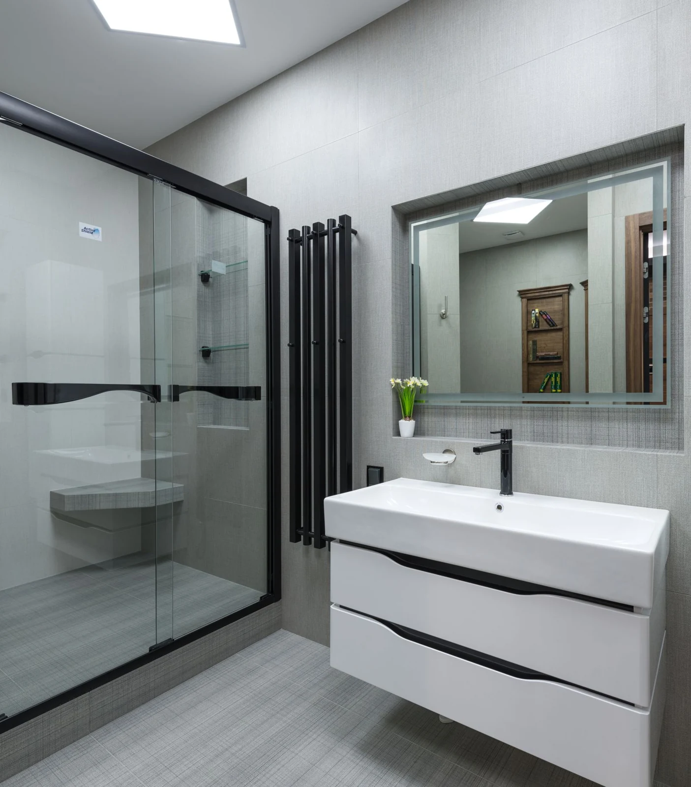 White sink with faucet at wall with mirror near glass shower cabin in stylish bathroom with glowing lights in apartment
