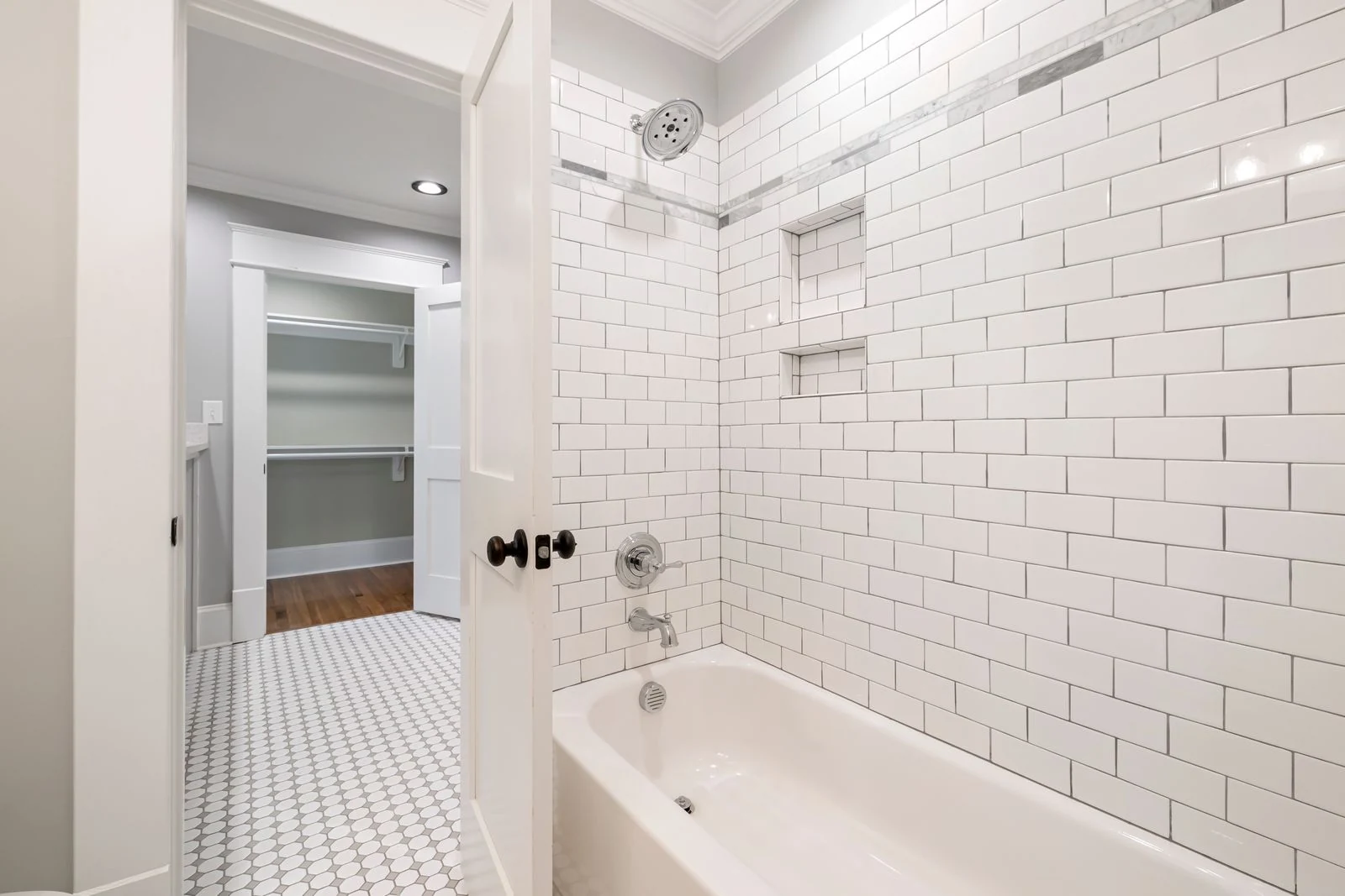 A modern bathroom featuring a white tiled bathtub and a view into an empty closet space